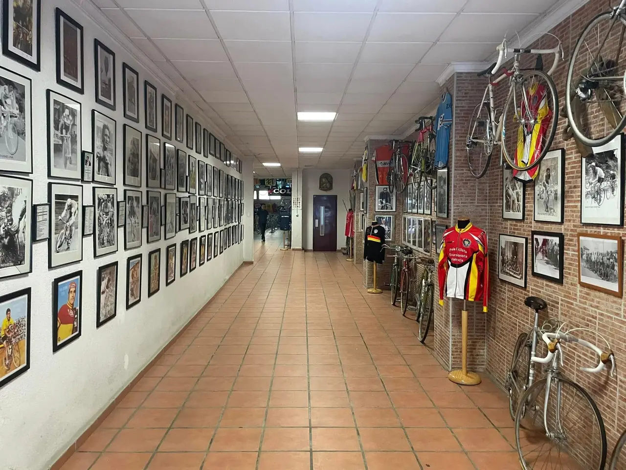 Pasillo de la sede del club, con las paredes cubiertas de fotografías enmarcadas, bicicletas de carretera colgadas y maniquíes con maillots históricos