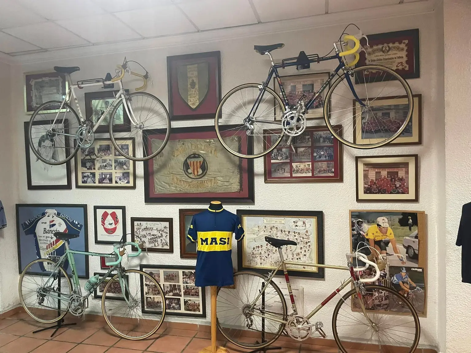 Banderín bordado de la Peña Ciclista Excursionista con la Senyera, entre dos bicicletas de carrera antiguas colgadas de la pared
